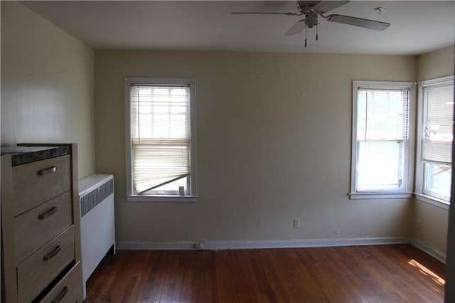 spare room featuring radiator, dark wood-type flooring, a wealth of natural light, and ceiling fan