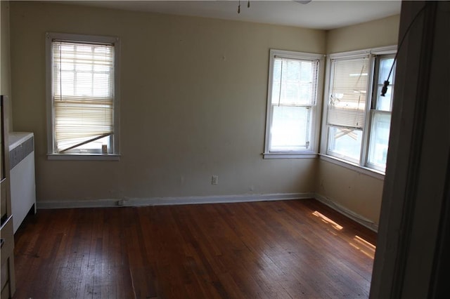 empty room with plenty of natural light, dark wood-type flooring, radiator heating unit, and ceiling fan