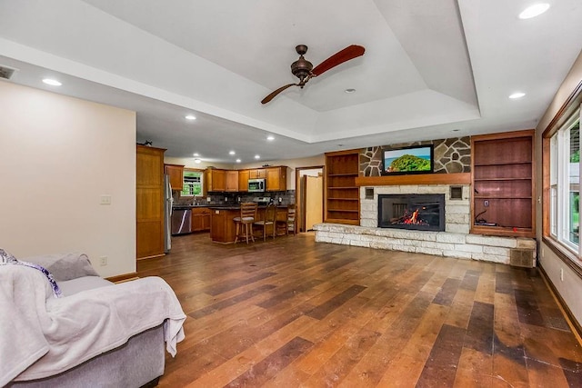 living room with a fireplace, built in features, hardwood / wood-style floors, ceiling fan, and a raised ceiling