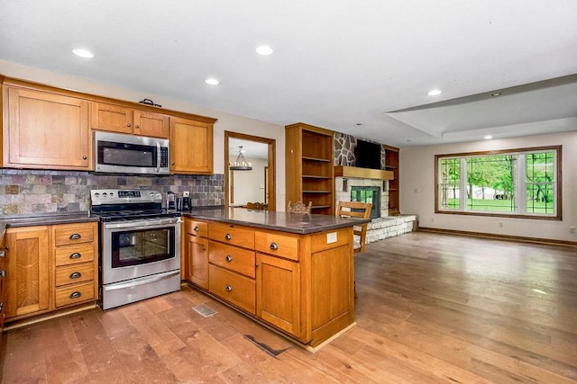 kitchen featuring appliances with stainless steel finishes, light hardwood / wood-style floors, a fireplace, and tasteful backsplash