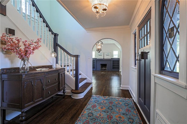 entryway with an inviting chandelier, dark wood-type flooring, ornamental molding, and a wealth of natural light