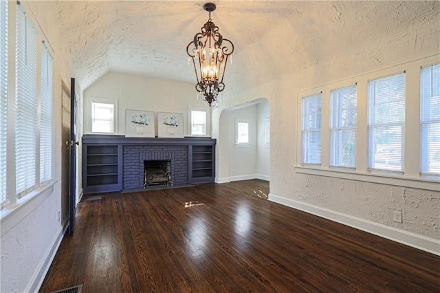 unfurnished living room with a brick fireplace, dark hardwood / wood-style flooring, a wealth of natural light, an inviting chandelier, and lofted ceiling