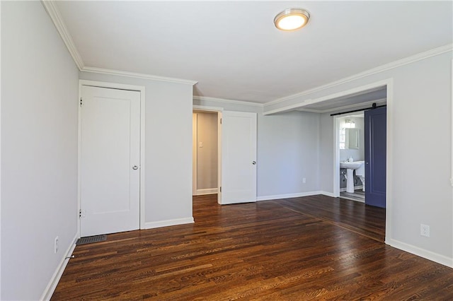 spare room featuring a barn door, ornamental molding, and dark hardwood / wood-style floors