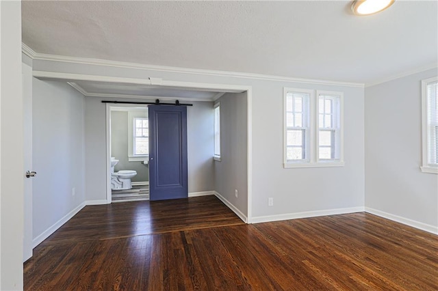 spare room featuring crown molding, a barn door, dark wood-type flooring, and a wealth of natural light