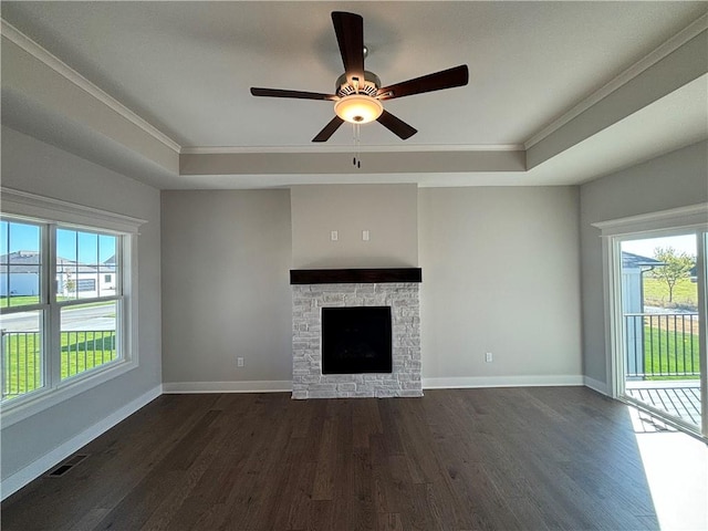 unfurnished living room with dark hardwood / wood-style flooring, a tray ceiling, a stone fireplace, and ornamental molding