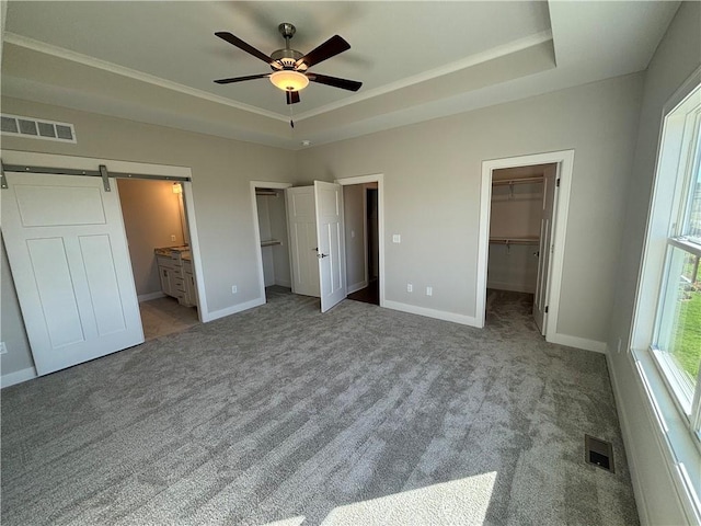 unfurnished bedroom featuring connected bathroom, a walk in closet, light colored carpet, a tray ceiling, and a barn door