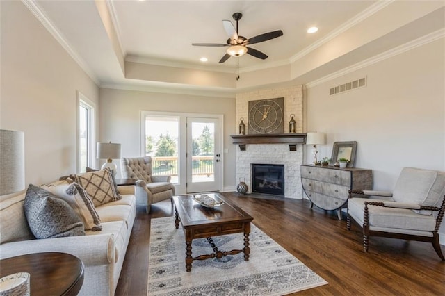 living room with crown molding, dark wood-type flooring, a fireplace, and a raised ceiling