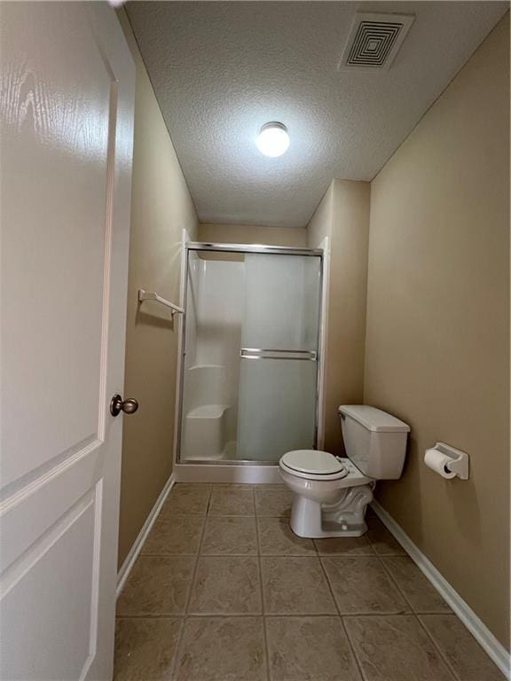 bathroom with a textured ceiling, a shower with shower door, toilet, and tile patterned flooring