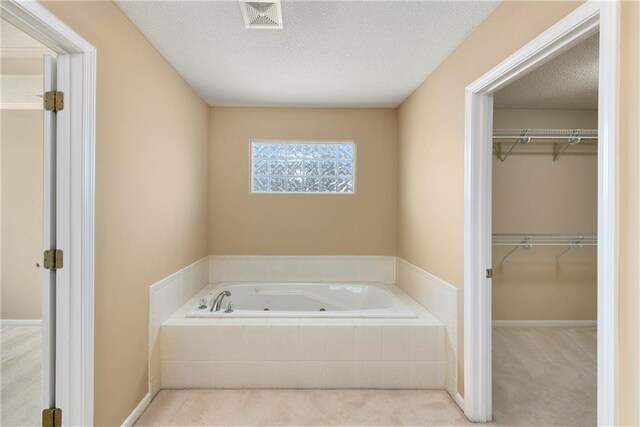 full bath with a textured ceiling, a spacious closet, a tub with jets, and visible vents