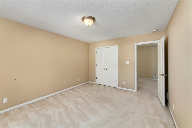 unfurnished bedroom featuring visible vents, baseboards, light colored carpet, a textured ceiling, and a closet