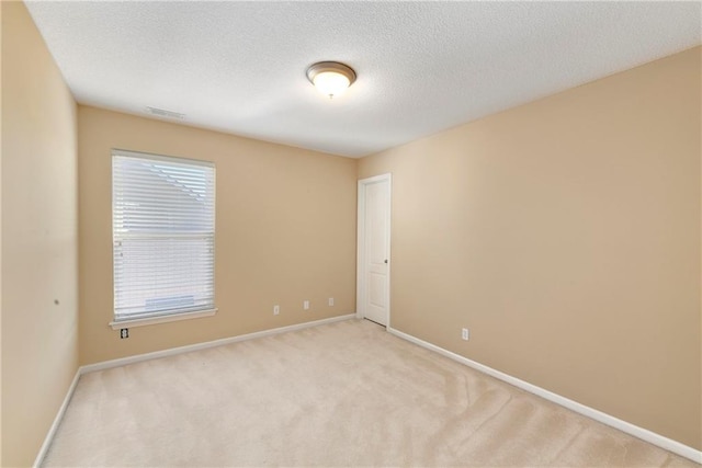 spare room featuring light carpet, a textured ceiling, and baseboards