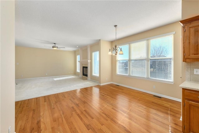 unfurnished living room with a textured ceiling, ceiling fan with notable chandelier, baseboards, light wood-style floors, and a glass covered fireplace