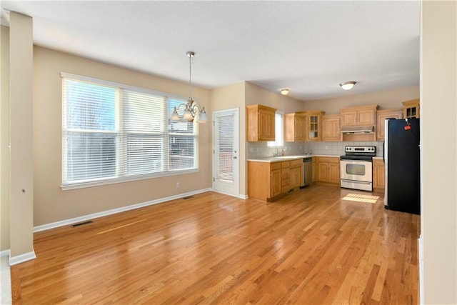 kitchen featuring light countertops, light wood-style flooring, backsplash, appliances with stainless steel finishes, and under cabinet range hood