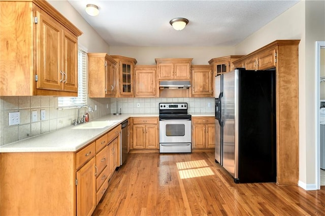 kitchen with under cabinet range hood, a sink, light countertops, appliances with stainless steel finishes, and light wood-type flooring