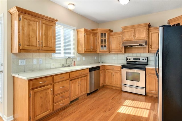 kitchen with light wood-style flooring, decorative backsplash, appliances with stainless steel finishes, a sink, and under cabinet range hood