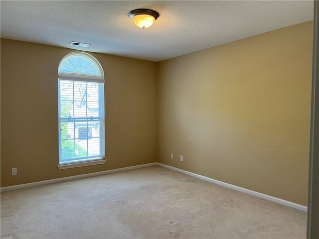 empty room with a textured ceiling, baseboards, visible vents, and light colored carpet