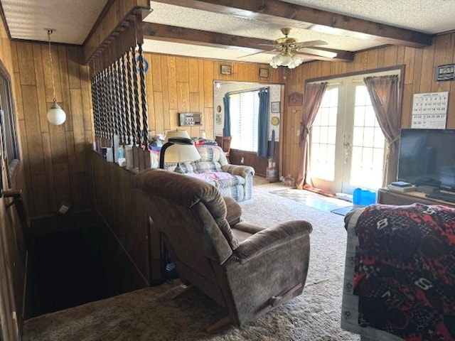 living room featuring wooden walls, beamed ceiling, dark carpet, french doors, and ceiling fan