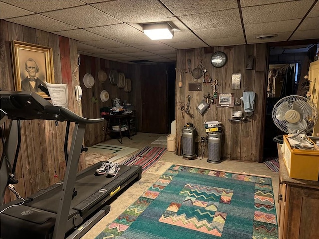 workout room featuring a drop ceiling, wooden walls, and carpet floors