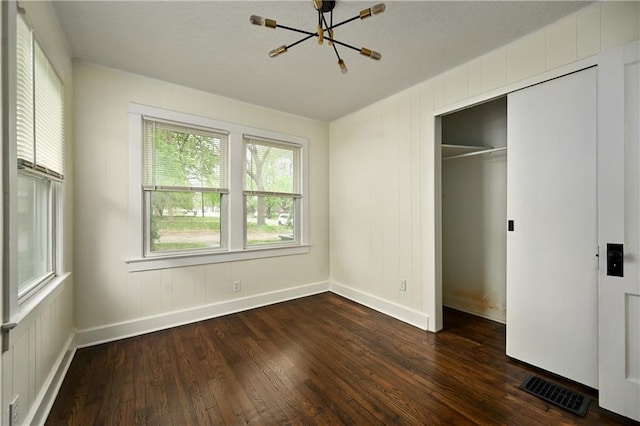 unfurnished bedroom with dark hardwood / wood-style flooring, a closet, and a notable chandelier