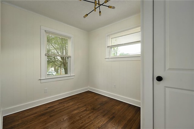 empty room with dark wood-type flooring, crown molding, and a notable chandelier