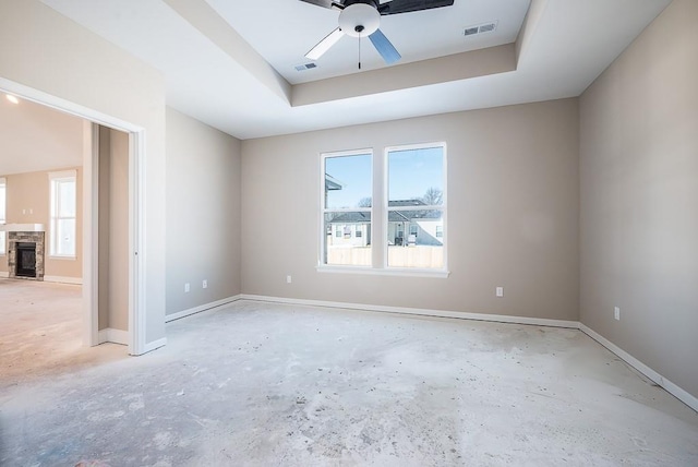 unfurnished room featuring ceiling fan, a stone fireplace, and a tray ceiling