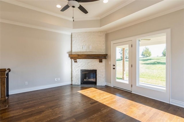 unfurnished living room featuring a stone fireplace, ornamental molding, ceiling fan, and dark hardwood / wood-style flooring