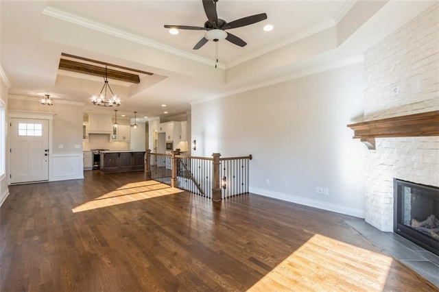 unfurnished living room featuring a raised ceiling, ornamental molding, dark hardwood / wood-style floors, ceiling fan with notable chandelier, and a fireplace