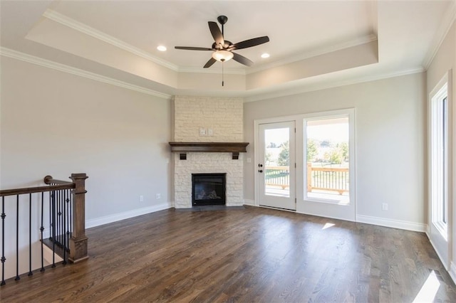 unfurnished living room featuring crown molding, a stone fireplace, a tray ceiling, and dark hardwood / wood-style floors