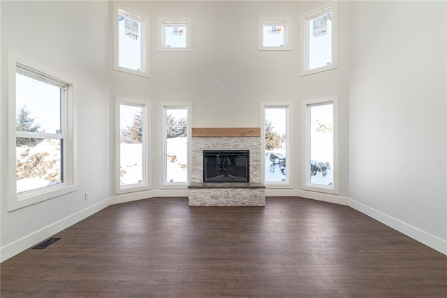 unfurnished living room featuring a stone fireplace, dark wood-style flooring, a wealth of natural light, and baseboards