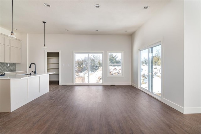 unfurnished living room with dark wood-style floors, a sink, and baseboards