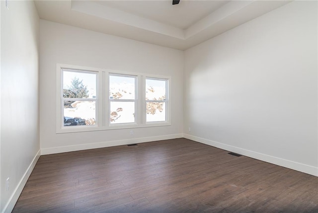 unfurnished room featuring a tray ceiling, dark wood finished floors, and baseboards