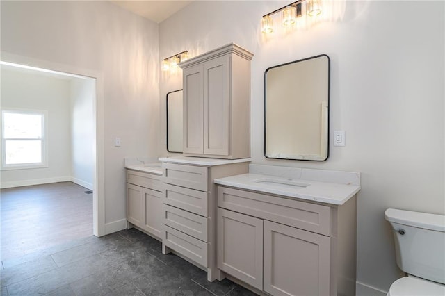 bathroom featuring baseboards, two vanities, and toilet