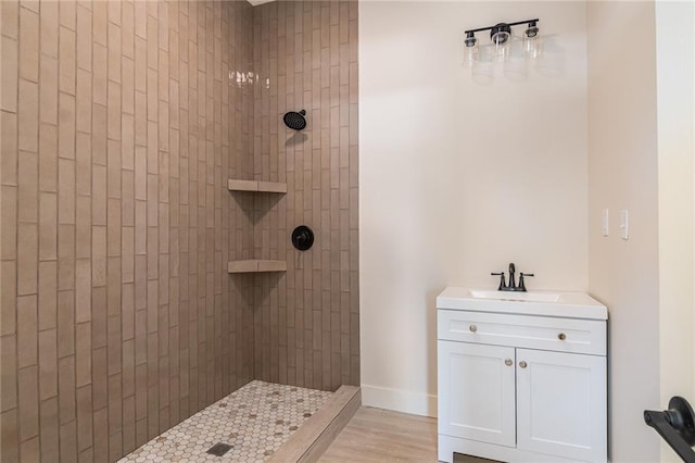 bathroom featuring a tile shower, vanity, baseboards, and wood finished floors