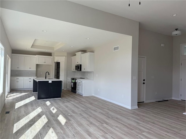 kitchen featuring white cabinets, decorative backsplash, a center island with sink, and black / electric stove