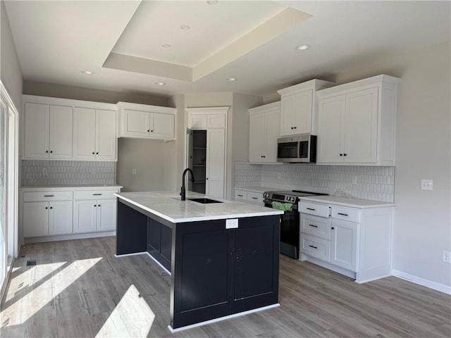 kitchen with a center island with sink, sink, light wood-type flooring, electric range oven, and white cabinetry