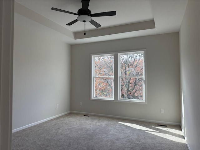 carpeted spare room with a raised ceiling and ceiling fan