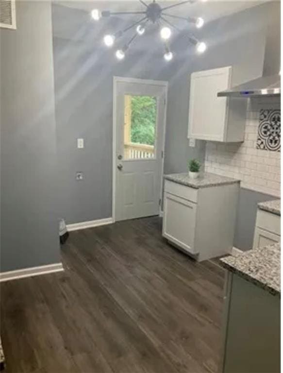 kitchen featuring white cabinets, wall chimney range hood, tasteful backsplash, dark hardwood / wood-style floors, and light stone countertops