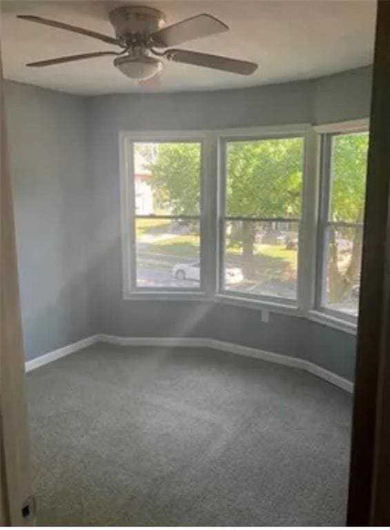 empty room featuring ceiling fan and dark carpet