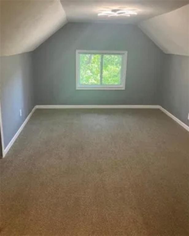 additional living space featuring lofted ceiling and dark carpet