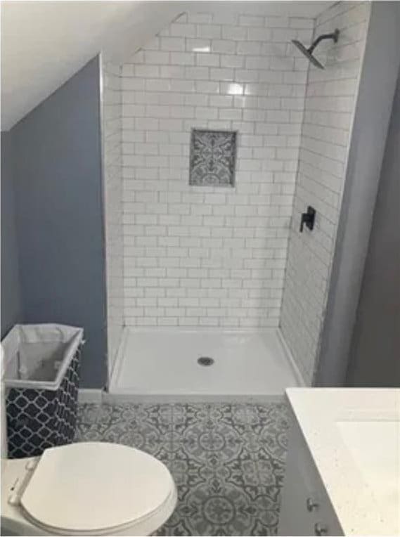 bathroom featuring toilet, tile floors, vanity, and a tile shower