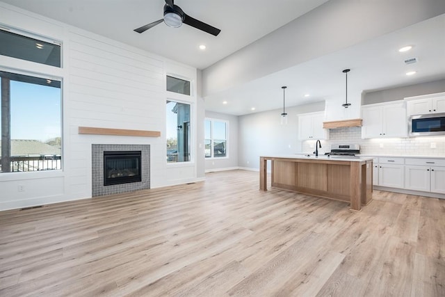 kitchen with an island with sink, white cabinetry, a wealth of natural light, decorative light fixtures, and stainless steel appliances