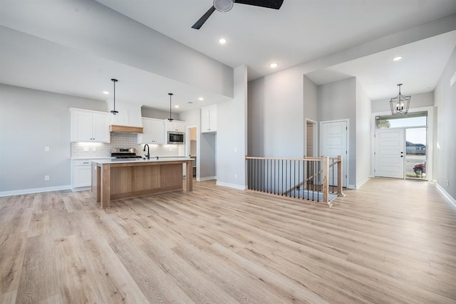 kitchen with hanging light fixtures, appliances with stainless steel finishes, white cabinetry, a kitchen island with sink, and light wood-type flooring