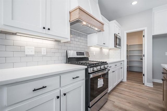 kitchen featuring light wood-type flooring, backsplash, stainless steel range with gas stovetop, white cabinetry, and custom exhaust hood