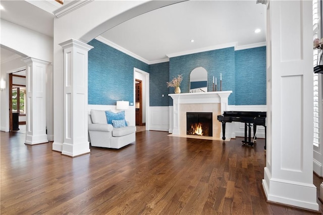 sitting room with decorative columns, a fireplace with flush hearth, arched walkways, wallpapered walls, and a wainscoted wall