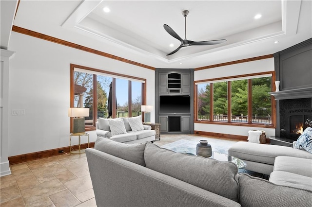 living room with a large fireplace, a ceiling fan, a raised ceiling, and baseboards