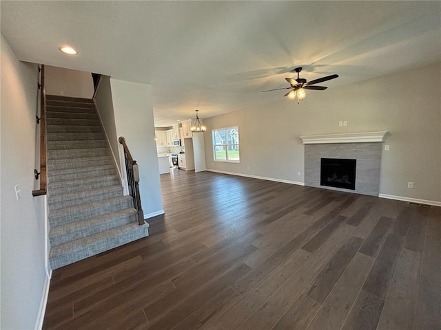 unfurnished living room with a fireplace, ceiling fan with notable chandelier, and dark wood-type flooring