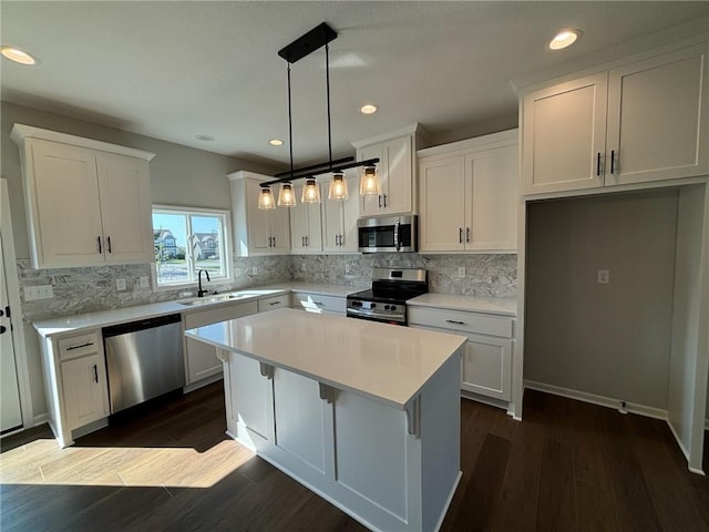 kitchen with stainless steel appliances, decorative light fixtures, white cabinets, dark hardwood / wood-style floors, and a kitchen island