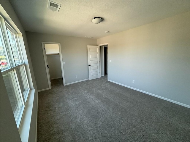 unfurnished bedroom featuring a walk in closet, a closet, dark carpet, and a textured ceiling