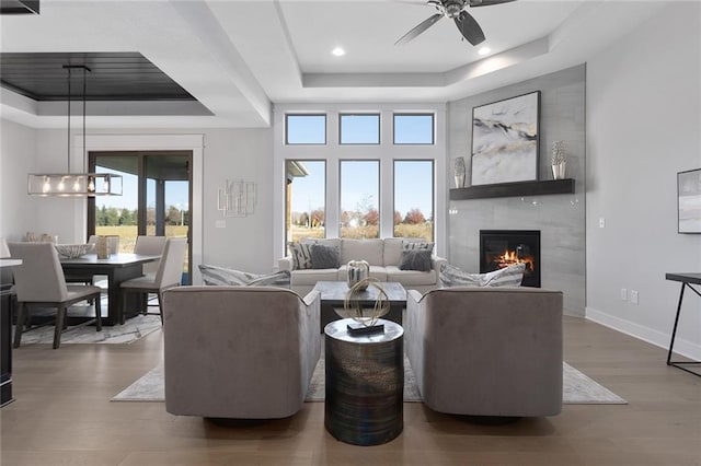 living room with a high end fireplace, hardwood / wood-style floors, a healthy amount of sunlight, and a raised ceiling