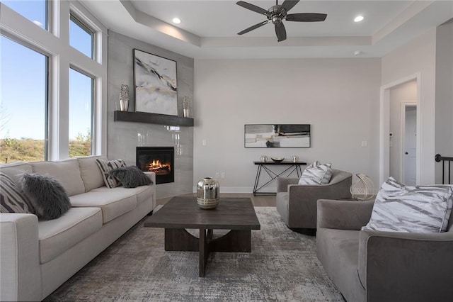 living room featuring ceiling fan, dark wood-type flooring, a fireplace, and a raised ceiling